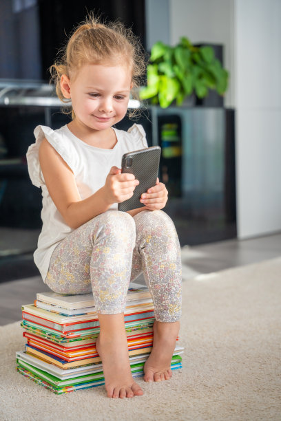小女孩坐在一堆儿童童话书上玩她的智能手机图片下载