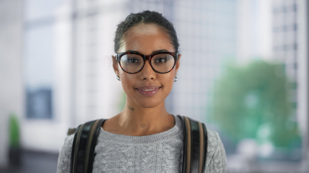 另类Z世代女性对着镜头微笑的肖像。年轻成功的黑人学生背着双肩包站在明亮的现代空间。教育与职业理念图片下载