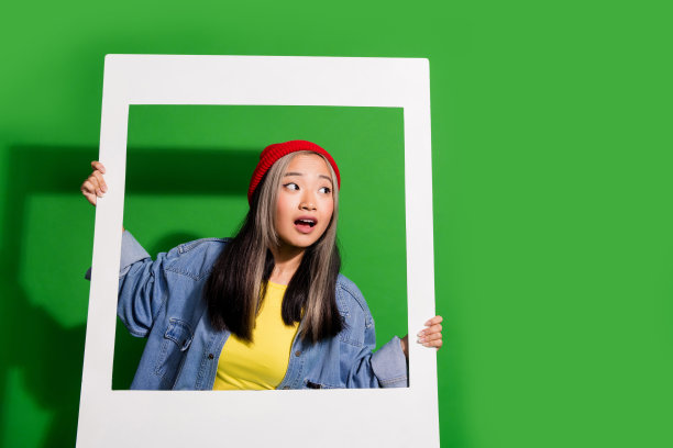 可爱的年轻女士的照片肖像拿着瞬间的框架，看着空白的空间，穿着时尚的牛仔服装，孤立在绿色背景上图片下载