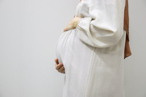 在白色孤立背景下的阿拉伯穆斯林孕妇触摸她的腹部，展示她怀孕9个月的身材图片下载