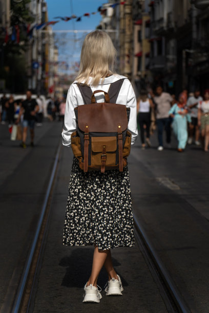 在一个阳光明媚的日子里，时尚的年轻女游客穿着白衬衫和裙子，背着手工背包站在伊斯坦布尔著名的Istiklal街中央，照片来自背后。旅行的概念图片下载