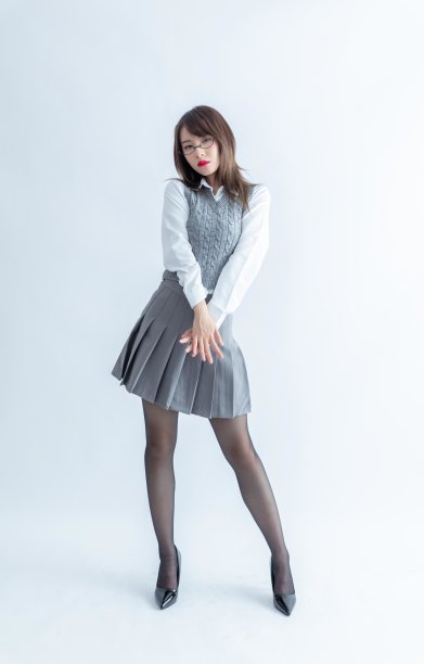一名身穿灰色百褶裙和白色衬衫的年轻女子双手交叉在胸前摆姿势。图片下载