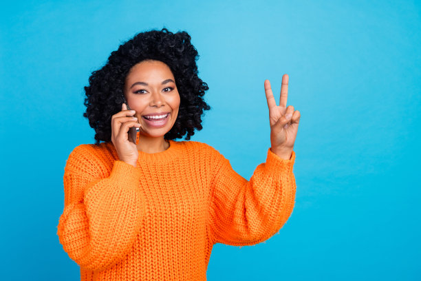 照片肖像漂亮的年轻女孩谈话电话节目v字穿时髦的针织衫橙色服装孤立的蓝色背景图片下载
