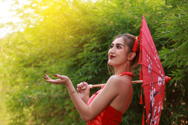 肖像美丽的亚洲妇女在中国旗袍旗袍与美丽的红色纸伞和红灯笼在森林背景，复制空间，中国新年的概念图片下载
