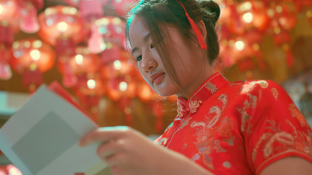 年轻，红发的亚洲女孩旗袍在中国寺庙里被授予金元宝。祝你新年吉祥快乐。图片下载