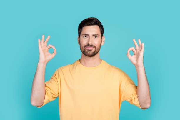 深色头发的帅哥穿着黄色t恤的人像照片展示了好符号双好孤立在青色背景图片下载