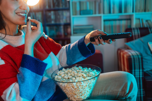 一个女人拿着电视遥控器吃爆米花的特写图片下载