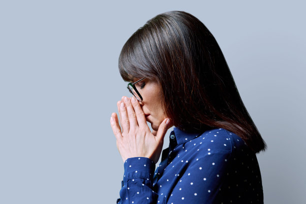成熟悲伤女人的侧面视图，闭上眼睛，双手合拢，灰色背景图片下载
