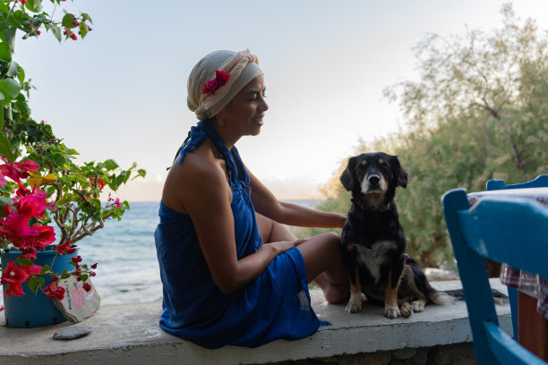 夏天，克里特岛南部一家典型的希腊酒馆里，穿着花衣服的美女抚摸着一只狗图片下载
