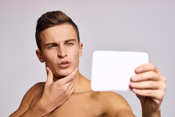 一个半裸的男人手里拿着一面镜子，审视着一张裁剪过的照片，背景是一张脸图片下载