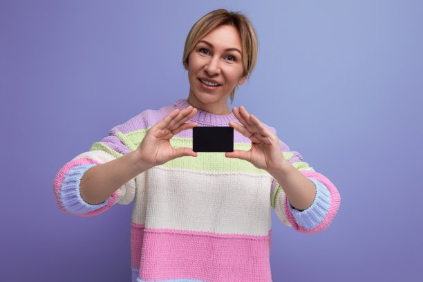 穿着休闲服装的金发碧眼的年轻女子在紫色的背景上展示了一张带有复制空间的信用卡模型图片下载