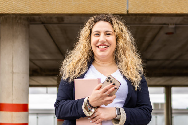 街上的女人拿着平板电脑和手机看着相机。穿着夹克的年轻女商人微笑着。图片下载