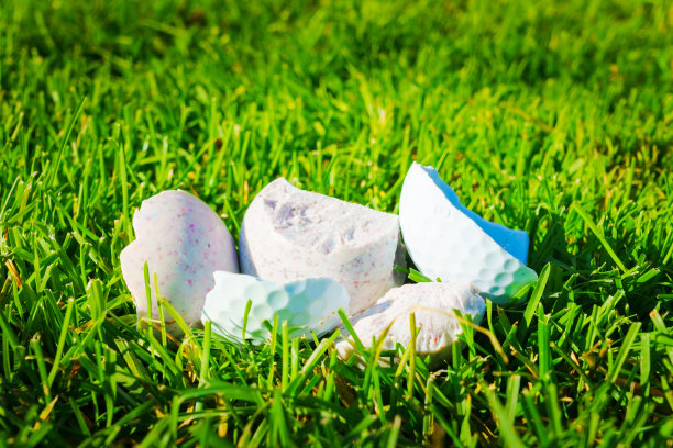 许多白色的高尔夫球碎片躺在绿色的草地上。损坏的高尔夫球，特写照片图片下载