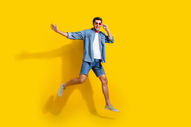 全身照片满意的愉快的男人穿着牛仔衬衫短裤飞行触摸太阳镜孤立在明亮的黄色背景图片下载