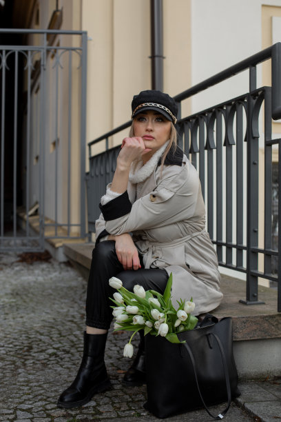 照片中的年轻女子戴着黑色的帽子，戴着白色的花，坐在篱笆旁看着镜头，大而美丽的眼睛图片下载