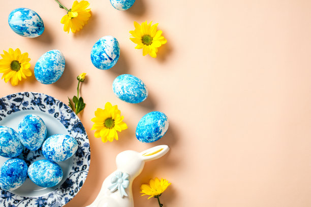 俯视图照片与盘子画复活节彩蛋，黄色的花，兔子在柔和的米色背景。图片下载