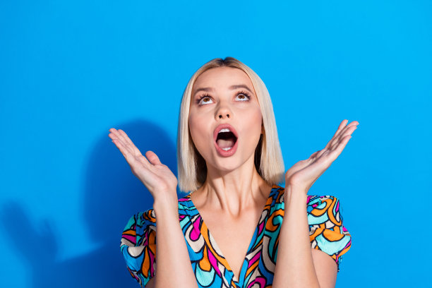 惊讶的漂亮女人穿着印花衬衫捕捉产品的照片，在明亮的蓝色背景上孤立的空白。图片下载