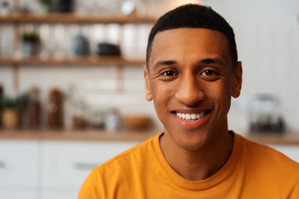 穿着黄色t恤的英俊微笑的非洲裔美国人，在家里的厨房里看着相机图片下载