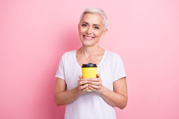 可爱的高级女士的照片肖像拿着纸咖啡杯享受休息，穿着时髦的白色服装孤立在粉红色的背景图片下载