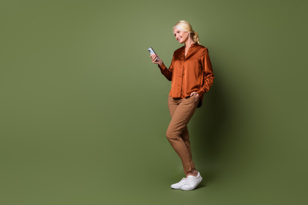 聪明积极的女人穿着丝绸衬衫裤子的全身照片，在绿色背景上阅读智能手机上的通知图片下载