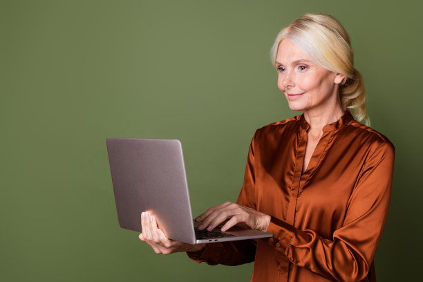 照片肖像漂亮的退休女性拿着上网本工作穿着时髦的棕色丝绸服装孤立的卡其色背景图片下载