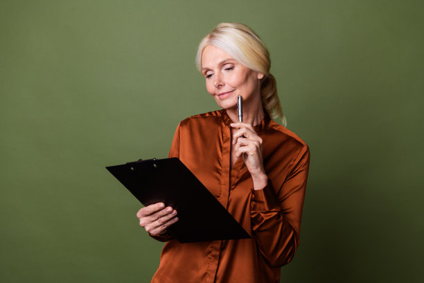 照片肖像有吸引力的退休妇女认为看纸持有人穿着时尚的棕色丝绸衣服孤立的卡其色背景图片下载