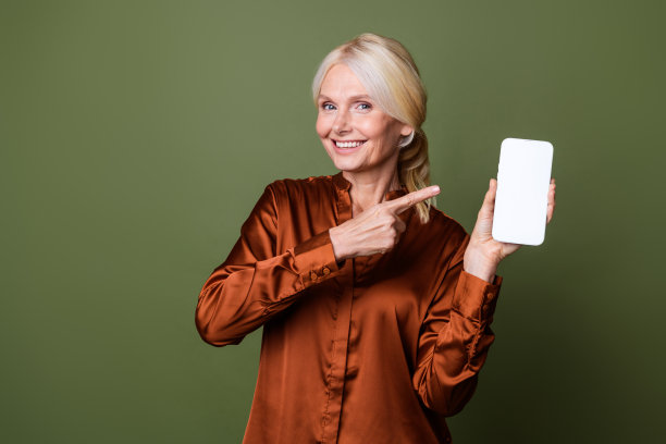 照片中，聪明开朗的女子穿着丝绸衬衫，在智能手机屏幕上指向商店，绿色背景上的空白空间被隔离开来图片下载