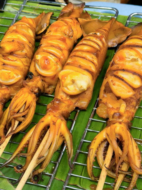 全画幅图片:金属烤架上一排排放在香蕉叶上的竹串上的烤海鲜串，煮熟的、有刻痕的、塞满鸡蛋的鱿鱼，触手上有圆形的粘性吸盘，高架视图图片下载