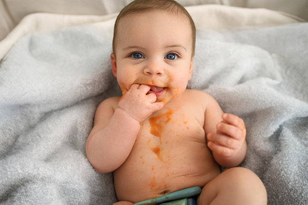 可爱可爱的婴儿滑稽肮脏的婴儿试图吃自己的水果或蔬菜泥涂抹在他的脸上。宝宝的第一份辅食。有机天然成分。婴儿食品概念。图片下载