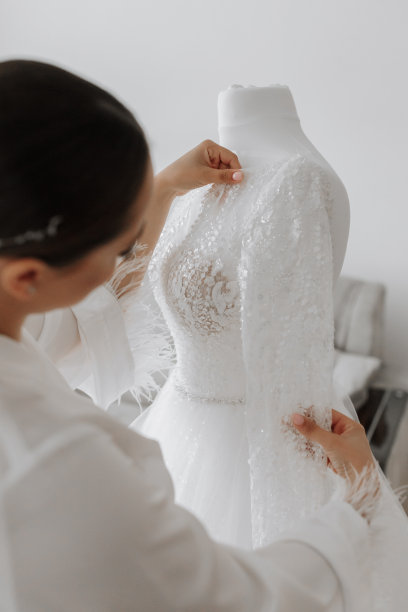 时尚的新娘，带着婚礼的发型和妆容，穿着白色的长袍站在她的婚纱旁边。手的特写照片图片下载