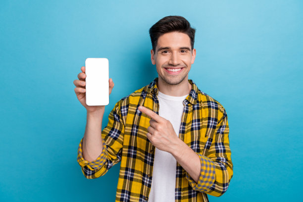照片中穿着格子衬衫的微笑开朗的商人手指着现代智能手机屏幕，蓝色背景的商店孤立图片下载