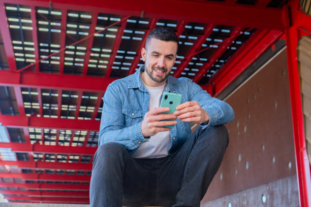 一个人坐在楼梯上玩智能手机，在外面微笑的照片。年轻人用手机发短信，积极快乐的态度看起来很酷图片下载