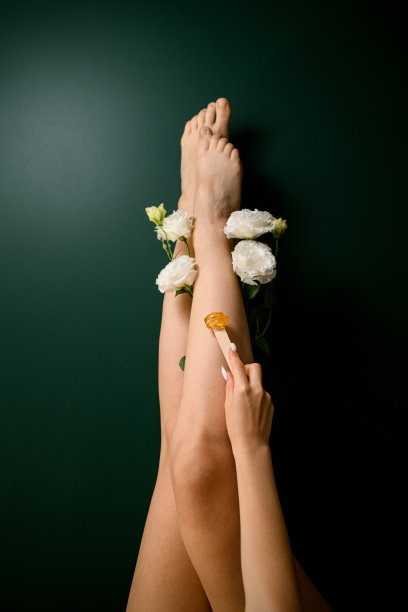 一个浅肤色的女人的腿与一个白色的精致玫瑰在绿色的背景图片下载