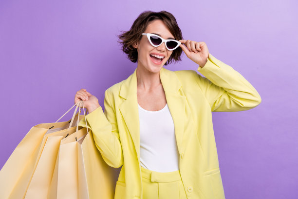 照片酷时尚的年轻模特穿着时髦的衣服触摸太阳镜拿着很多包购物商店孤立的紫罗兰色背景图片下载