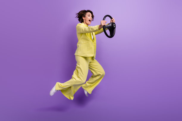 时髦漂亮的女人穿着黄色夹克跳高骑行车辆孤立的紫色背景的全长照片图片下载