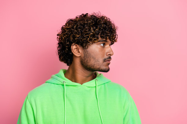 侧面资料照片自信的印度男子绿色运动衫看空空间卷发护理广告孤立的粉红色背景图片下载