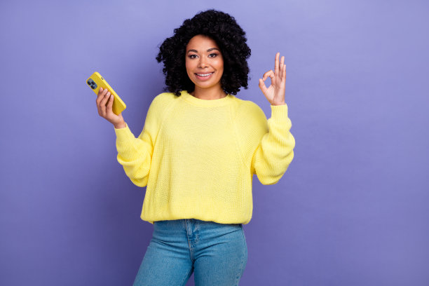 可爱的年轻女士的照片肖像拿着小玩意，显示出好的标志，穿着时髦的黄色衣服，孤立在紫色的背景上图片下载