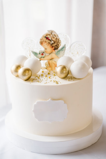 时髦的洗礼蛋糕与人物天使与翅膀和金色装饰。庆祝洗礼的概念。宝宝生日派对上的美味招待。蛋糕上的背景白色照片区。特写镜头。侧视图。图片下载