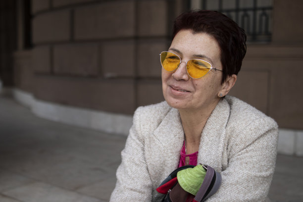 一位留着红色短发、戴着黄色太阳镜的多种族中年妇女，在城里走了很长一段路后，在车上坐了下来。休闲优雅的风格。x世代。真实的人，下班后。春天开始的股票照片图片下载