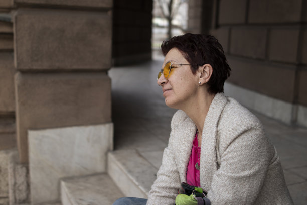 一位留着红色短发、戴着黄色太阳镜的多种族中年妇女，在城里走了很长一段路后，在车上坐了下来。休闲优雅的风格。x世代。真实的人，下班后。春天开始的股票照片图片下载