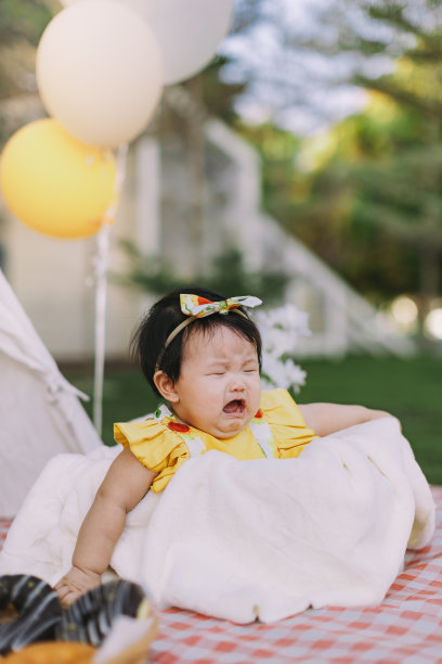 一个亚洲女婴坐在花园公园野餐垫子上的篮子里哭泣。库存图片图片下载