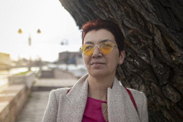 一位留着红色短发、戴着黄色太阳镜的多种族中年妇女，在镇上散步了很长时间。享受和微笑。休闲优雅的风格。x世代。真实的人，下班后。春天开始的股票照片图片下载