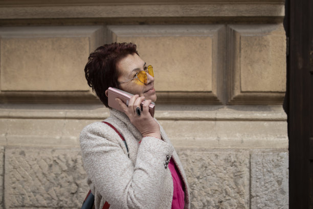 一位留着红色短发、戴着黄色太阳镜的多种族中年妇女，在镇上散步了很长时间。打电话。休闲优雅的风格。x世代。真实的人，下班后。春天开始的股票照片图片下载