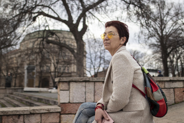 一位留着红色短发、戴着黄色太阳镜的多种族中年妇女，在城里走了很长一段路后，在车上坐了下来。休闲优雅的风格。x世代。真实的人，下班后。春天开始的股票照片图片下载