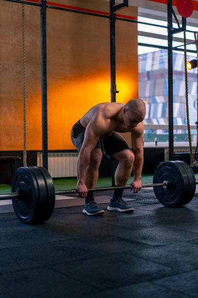 在一个体育俱乐部里，一个秃顶的教练穿着运动短裤在杠铃上举重图片下载