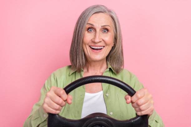 照片积极开朗好心情的祖母穿着绿色时尚的衣服开着新的自己的跑车孤立在粉红色的背景图片下载