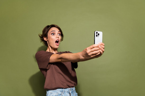 照片上的年轻美女看起来吓坏了，设备屏幕上穿着时髦的棕色衣服，孤立在卡其色背景上图片下载