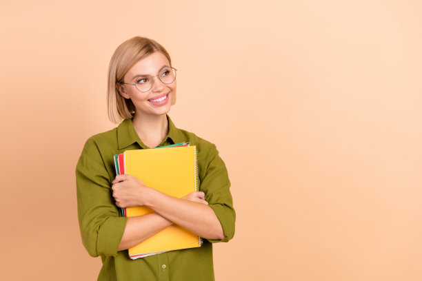 开朗的女孩肖像穿着卡其色衬衫，戴着眼镜，拥抱着书，在柔和的色彩背景上提供孤立的空白空间图片下载