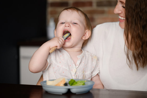 可爱的孩子坐在妈妈的怀里，用勺子独立地吃着健康的切碎的蔬菜泥。自饲理念，辅食图片下载