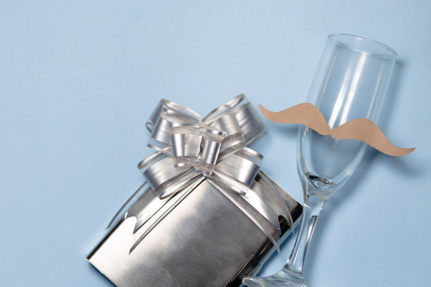 一个留着小胡子的玻璃杯，杯边是一个装在灰色发亮盒子里的礼物。父亲节。copyspace图片下载